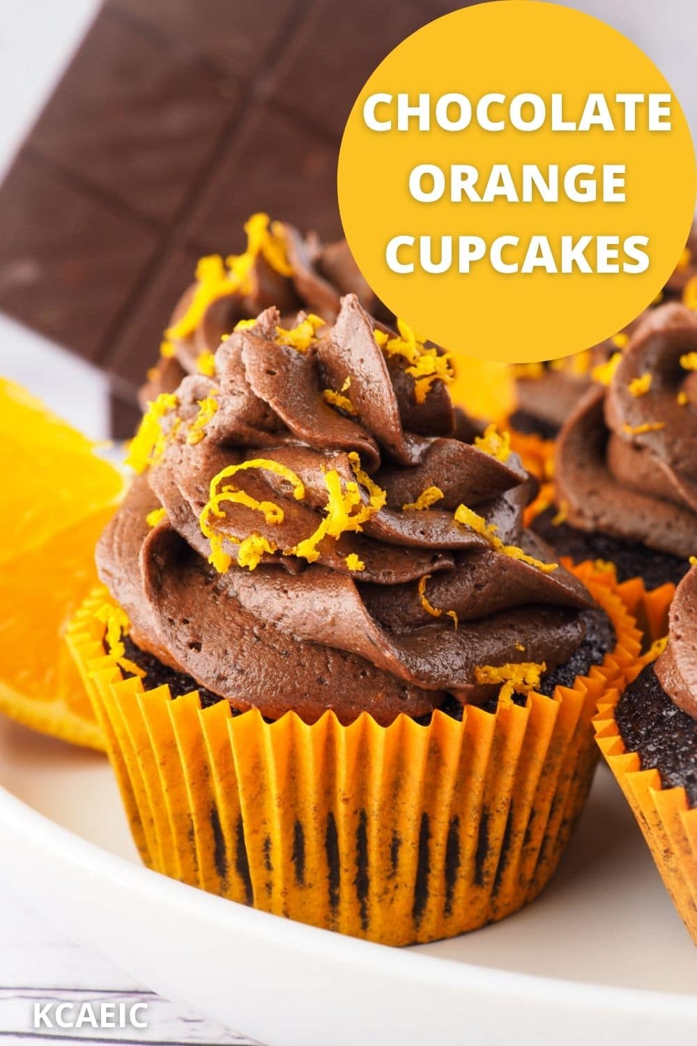 Chocolate Orange Cupcakes 11 Cupcakes on a plate with fresh oranges and chocolate in the background, with text overlay chocolate orange cupcakes and KCAEIC.