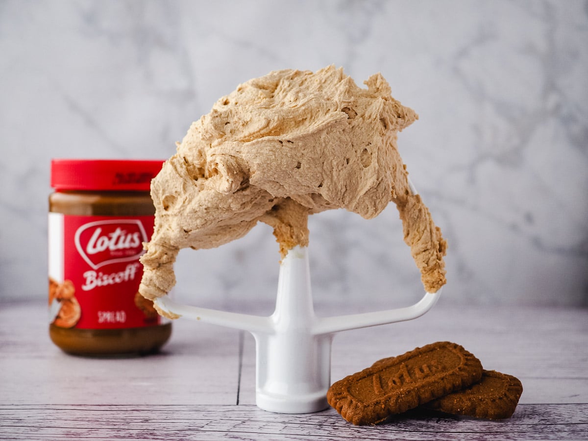 Buttercream on beater with biscuits to the side and jar of spread in background.