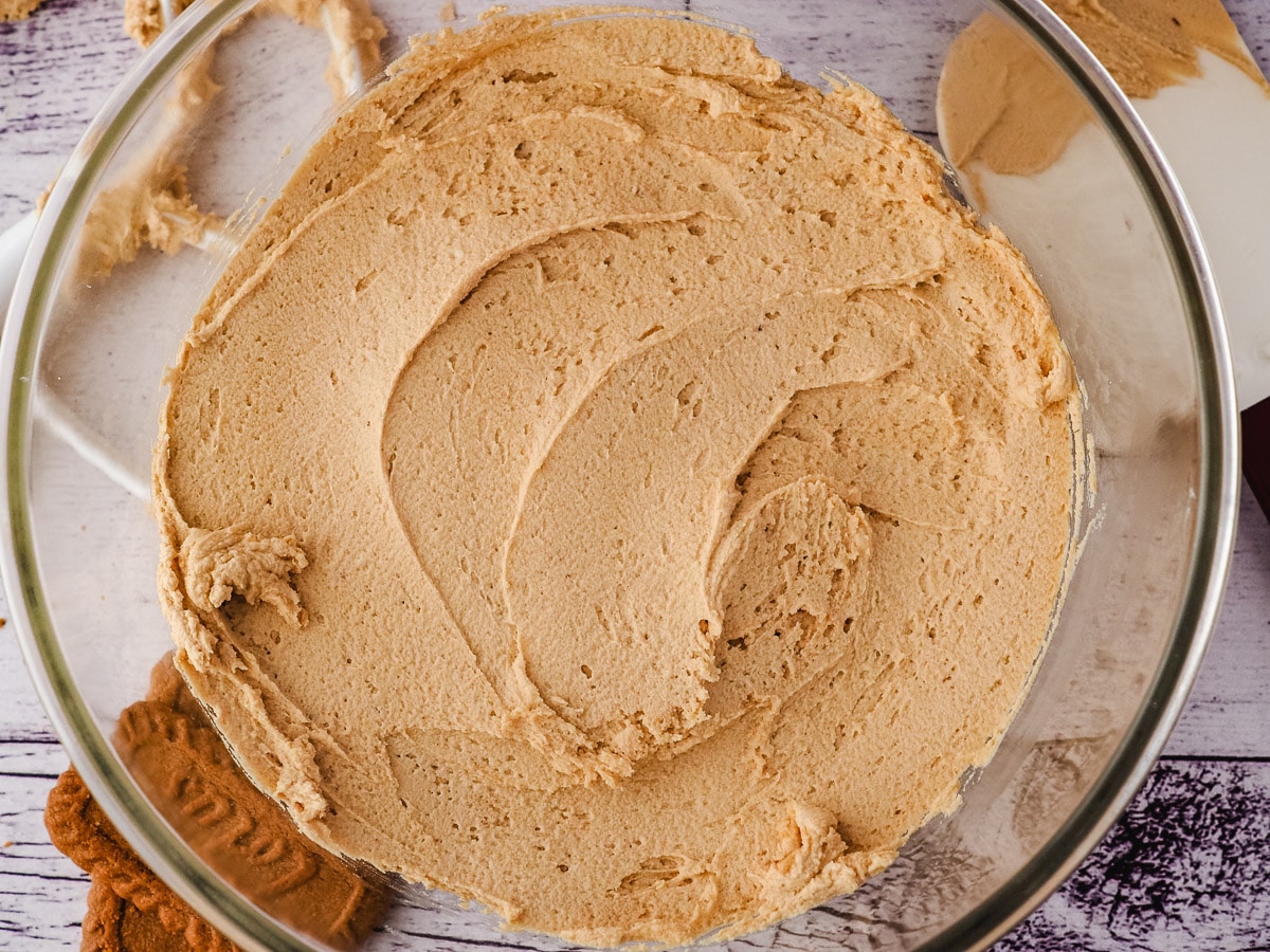 Buttercream in clear bowl with beater, spatula and biscuits to the side.