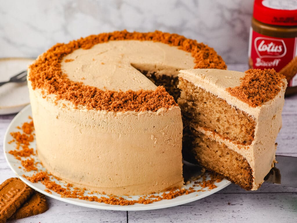 Biscoff cake decorated with frosting, with biscuits and jar of spread in background.