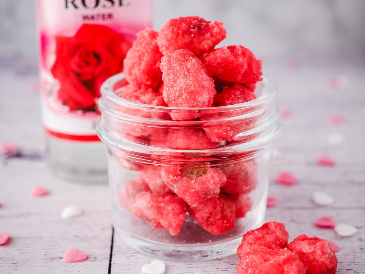 Pralines Roses 4 Small mason jar filled with pralines, surrounded by hear sprinkles, with rose water in the background.