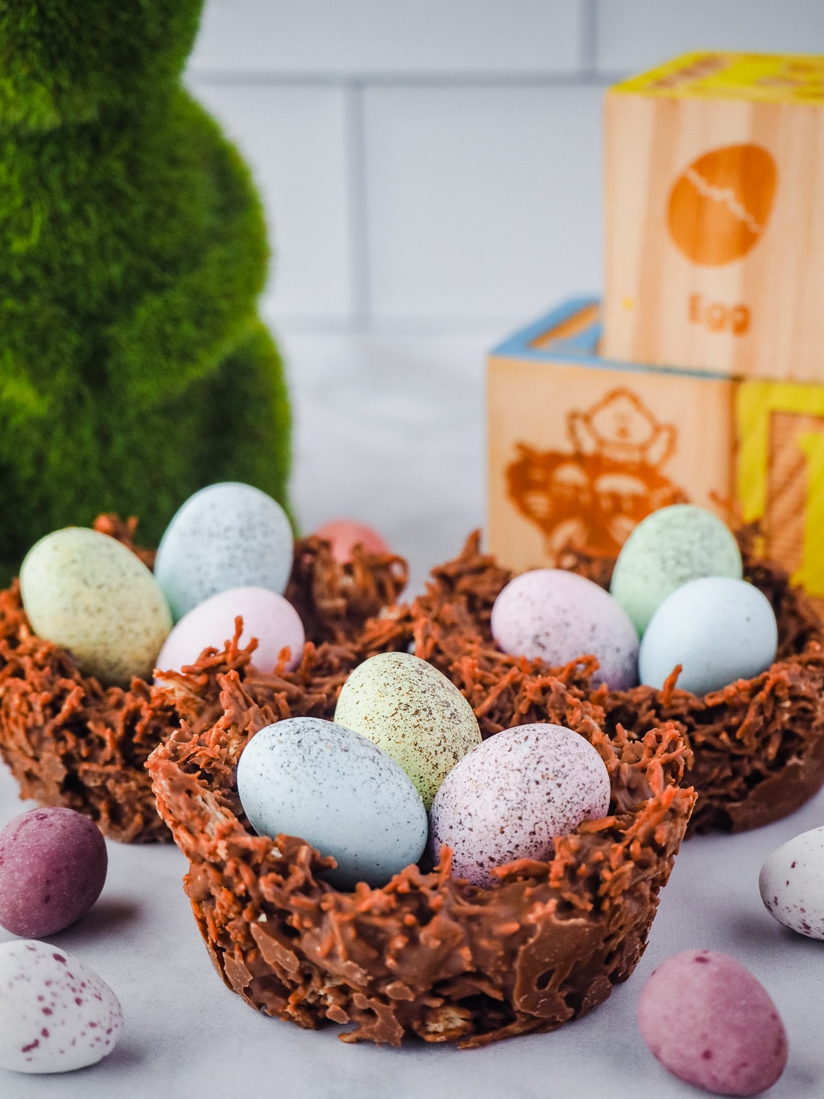 Nests surrounded by mini eggs, with bunny and Easter blocks in background.