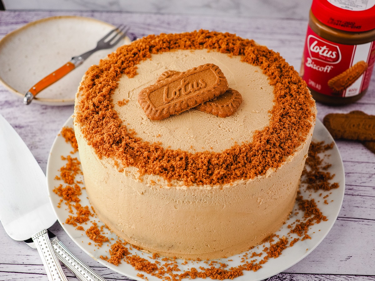 Whole cake on a plate, with serving ware, jar of biscoff spread and serving plate and fork on the side.