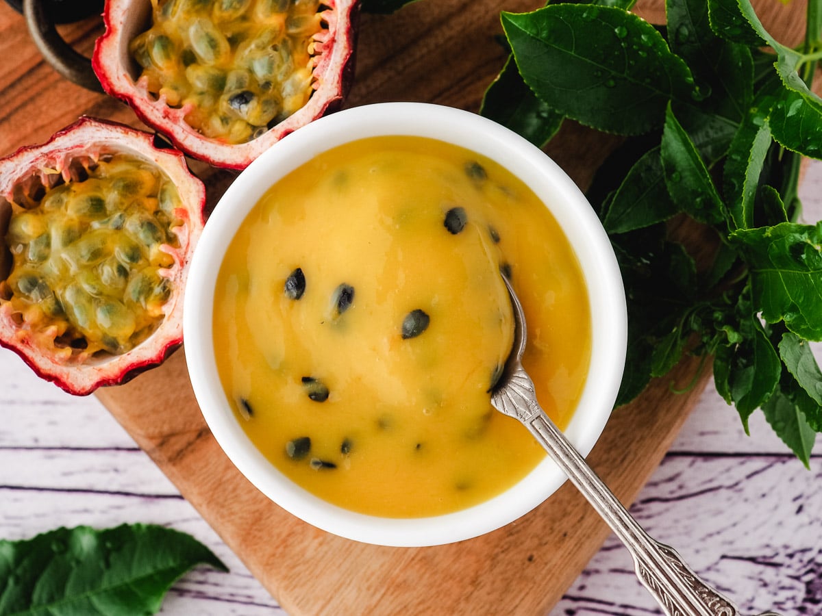 Curd in a serving bowl with a spoon, with fresh passion fruit and leaves on the side.