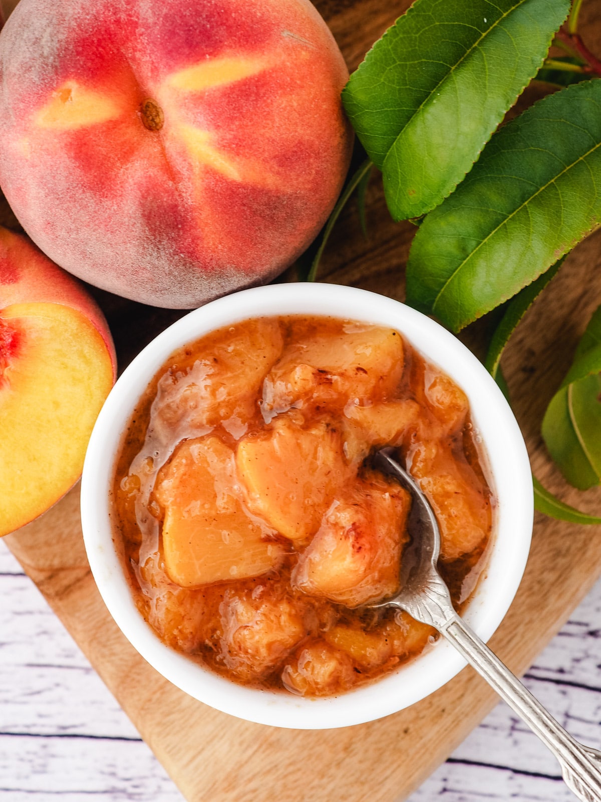 Peach compote 11 Compote in serving bowl with spoon and fresh peaches.