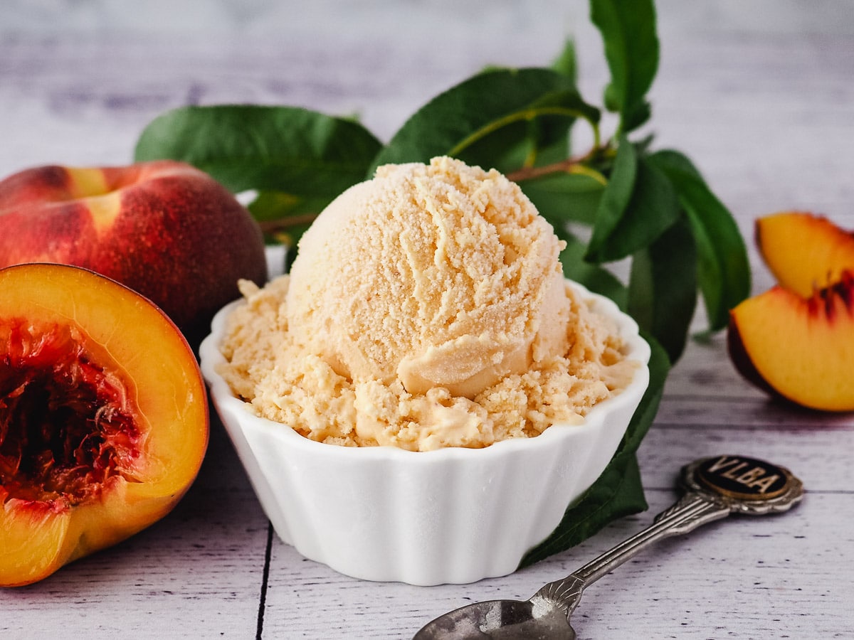 Scoop of ice cream in a bowl with a spoon and fresh peaches.