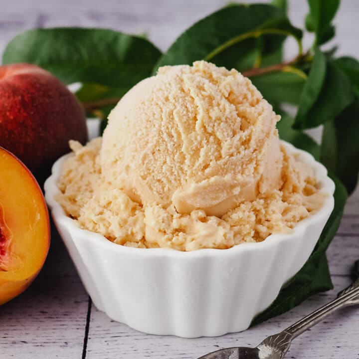 Close up scoop of ice cream in a bowl with spoon, fresh peaches and peach leaves.