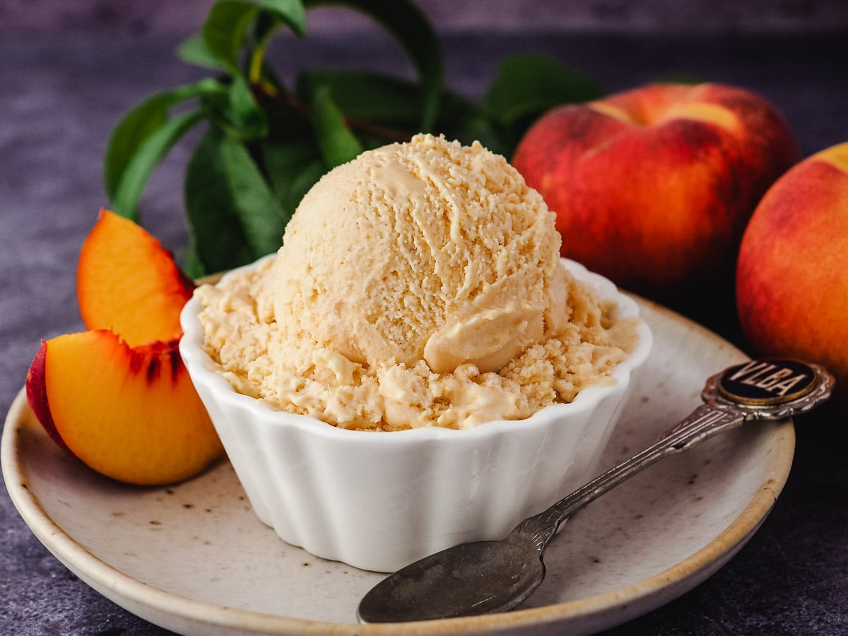Scoop of ice cream with spoon on a plate, with fresh peaches.