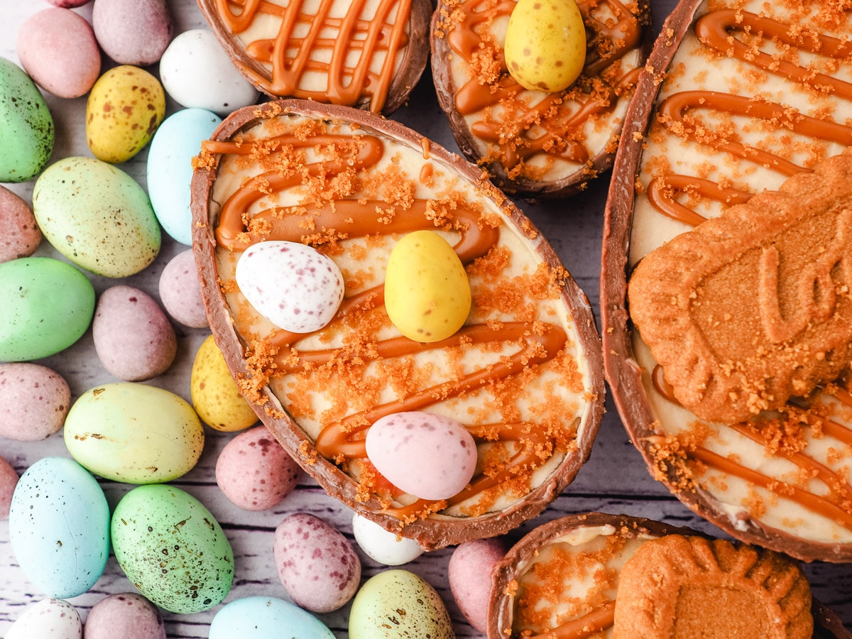 Cheesecake decorated with drizzled Biscoff spread, mini eggs and crumbs, with colorful mini eggs on the side.