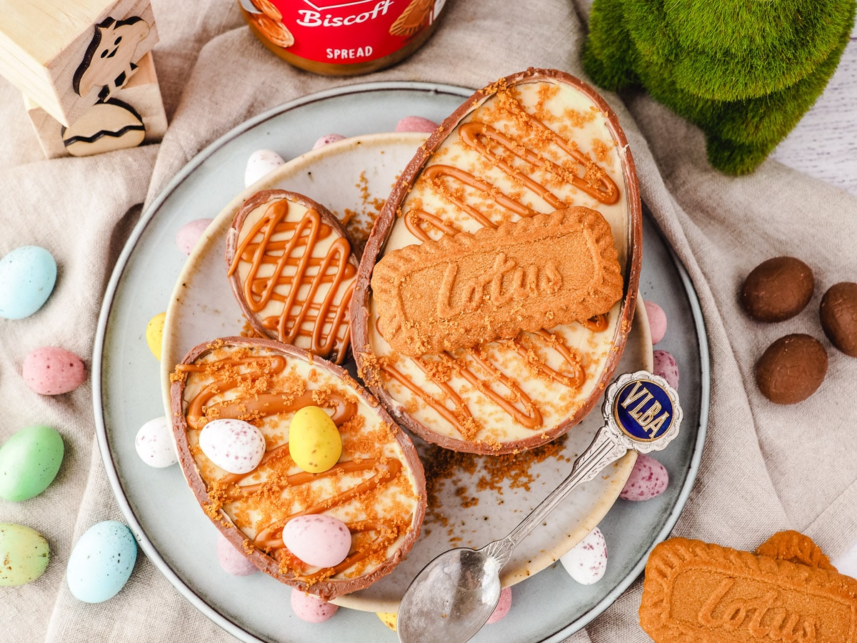 Large, medium and small cheesecake eggs on a plate with a spoon, surrounded by colorful mini eggs.