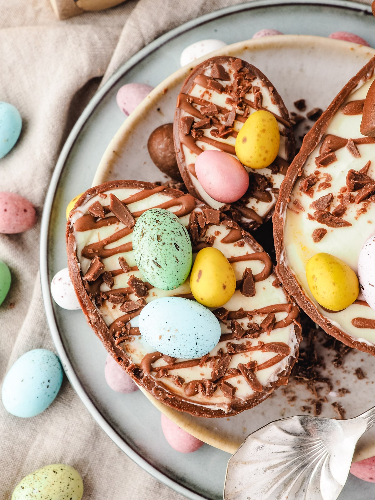 Close up medium, small and large cheesecakes on a plate with mini eggs and a spoon.