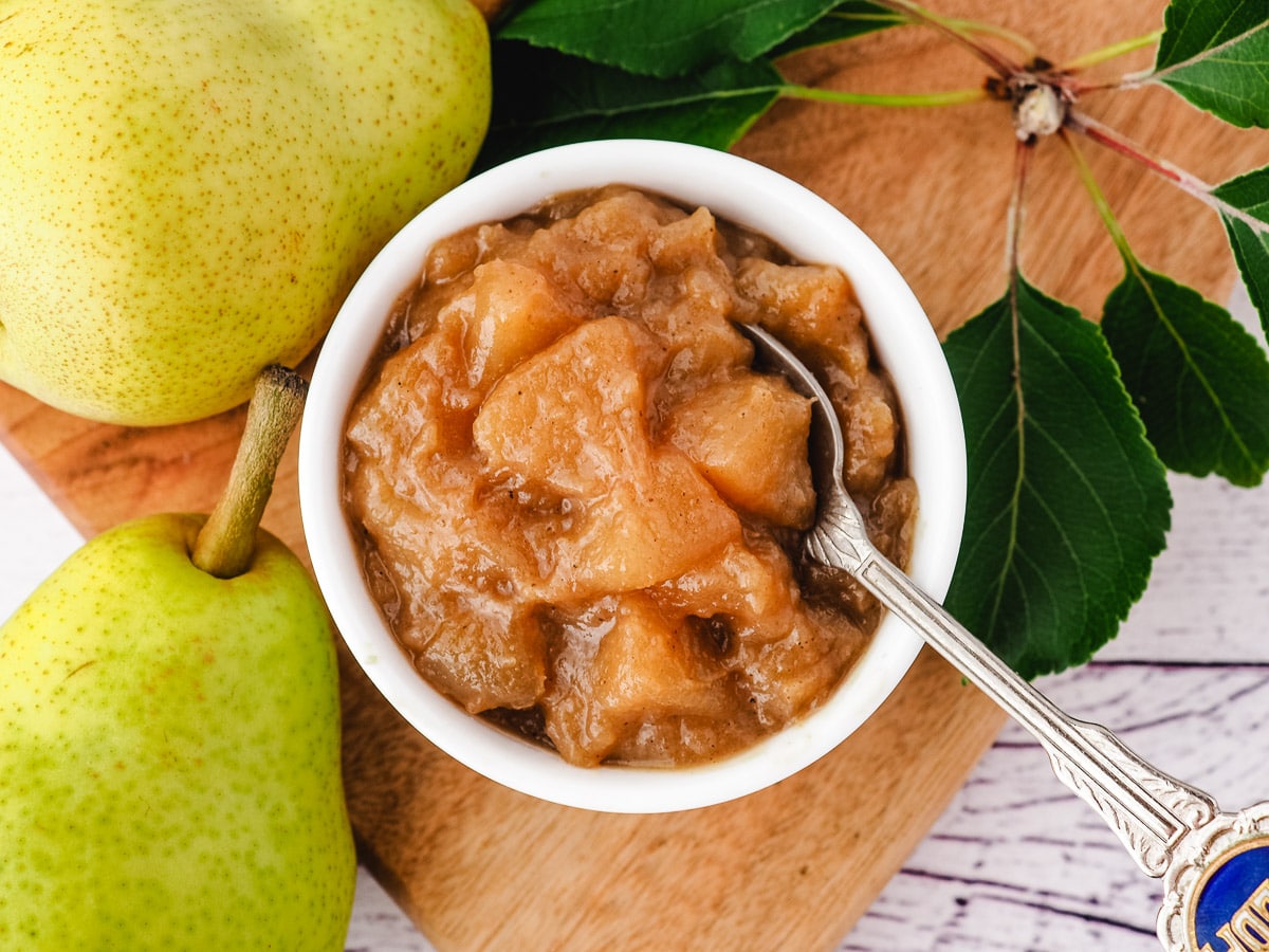 Compote in a serving bowl with a spoon, and fresh pears and leave on the side.