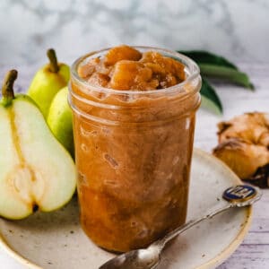 Mason jar of compote, with spoon and fresh pears and ginger on the side.