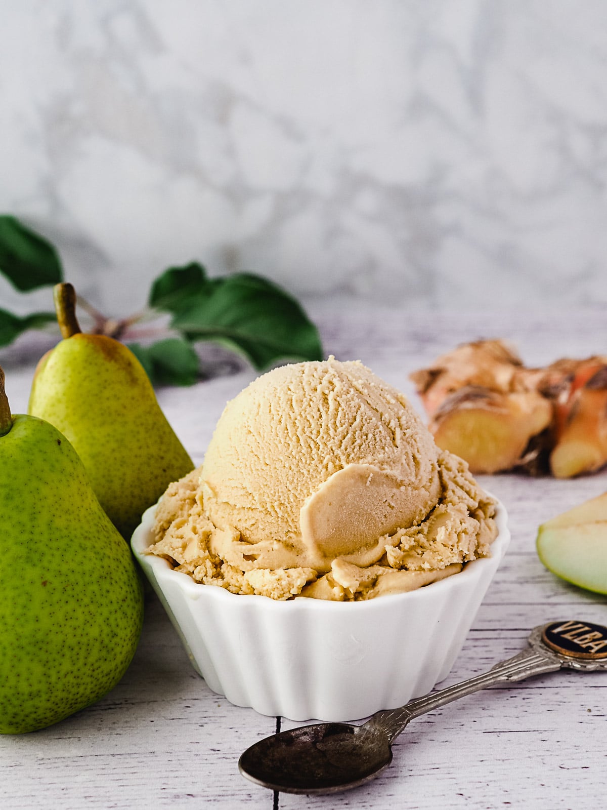 Scoop of pear ice cream with spoon, fresh pears and fresh ginger on the side.