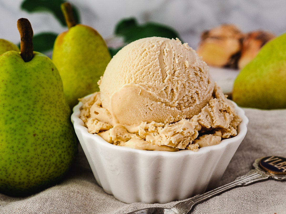 Scoop of pear ice cream with spoon, fresh pears and fresh ginger on the side.