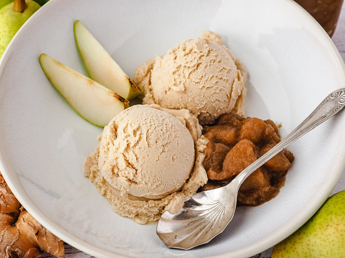 Serving of scoops of pear ice cream in a bowl, with fresh pears, pear compote and a spoon.