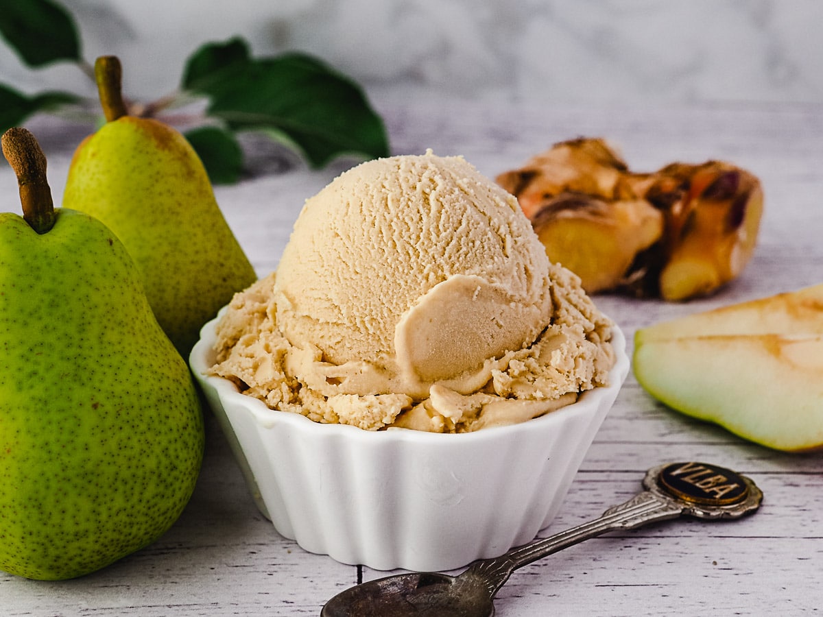 Scoop of pear ice cream with spoon, fresh pears and fresh ginger on the side.