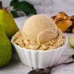 Scoop of pear ice cream with spoon, fresh pears and fresh ginger on the side.