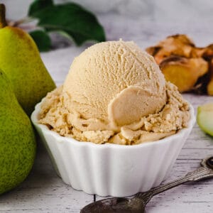 Scoop of pear ice cream with spoon, fresh pears and fresh ginger on the side.