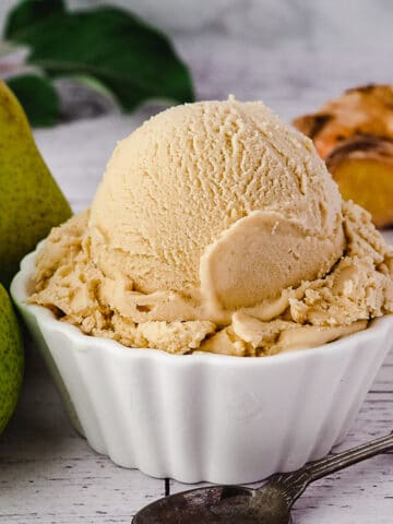 Scoop of pear ice cream with spoon, fresh pears and fresh ginger on the side.