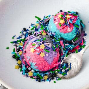 Close up two scoops of ice cream with space sprinkles in a bowl with a spoon.