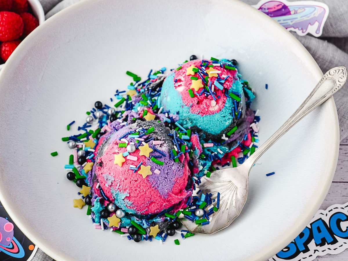 Two scoops of ice cream with space sprinkles in a bowl with a spoon, surrounded by space stickers.