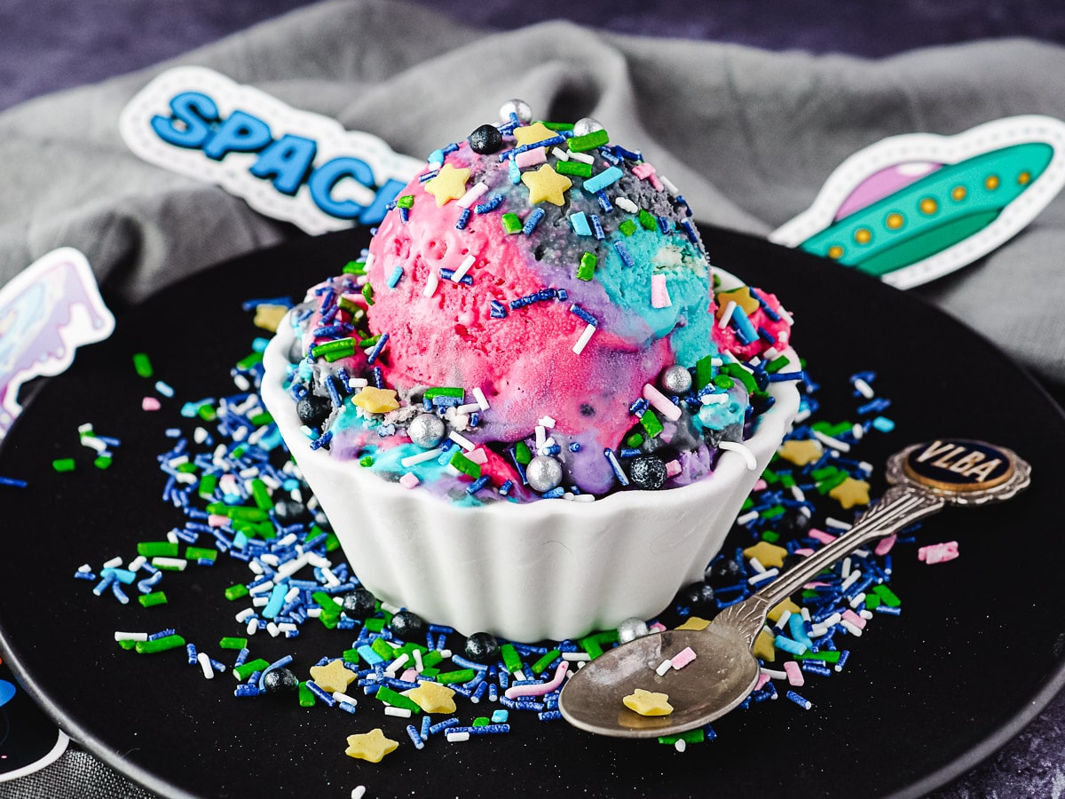 Galaxy Ice Cream 3 Scoop of ice cream with sprinkles, on a plate with spoon and sprinkles, and space in the background.