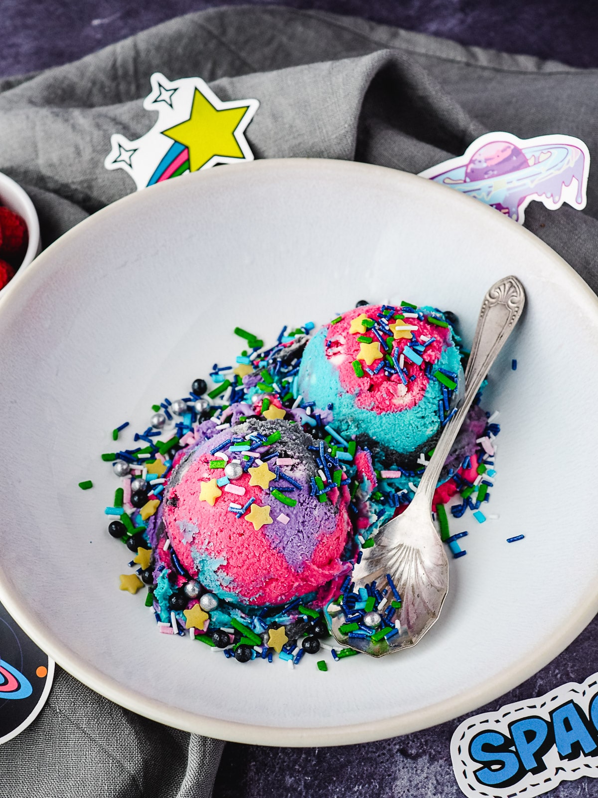 Two scoops of ice cream with space sprinkles in a bowl with a spoon, surrounded by space stickers.