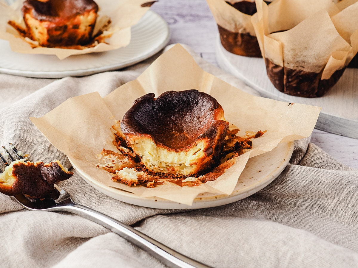 Mini Burnt Cheesecake 9 Mini cheesecake on a plate with a piece taken out with a fork, rest of cheesecakes in the background.