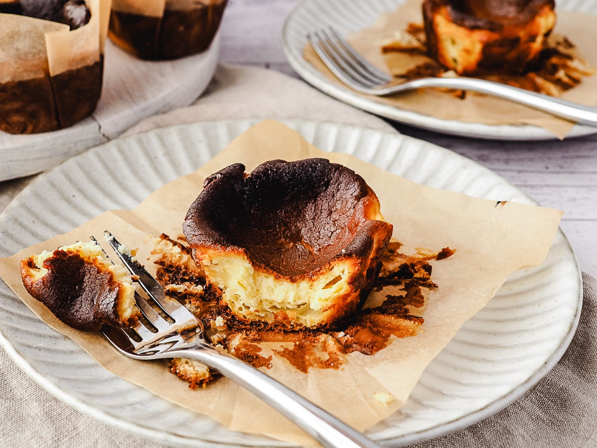 Mini Burnt Cheesecake 2 Mini cheesecake on a plate with a piece taken out with a fork, rest of cheesecakes in background.