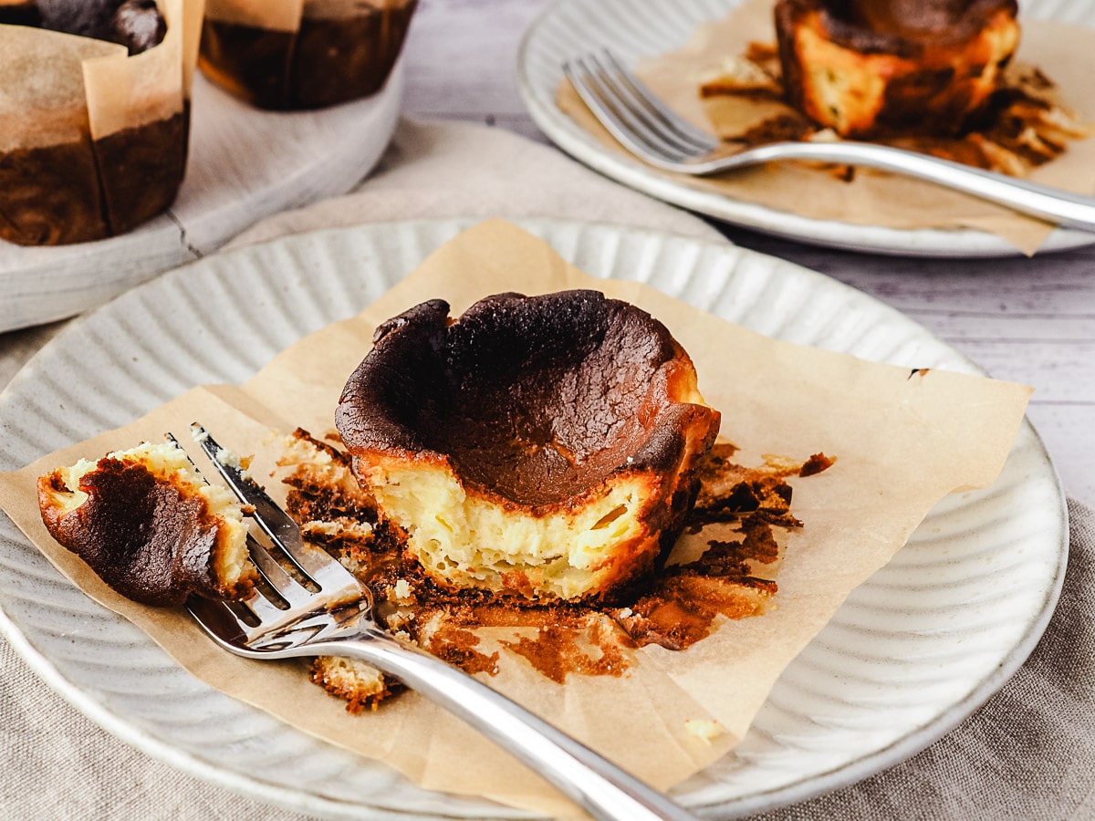 Mini cheesecake on a plate with a piece taken out with a fork, rest of cheesecakes in background.