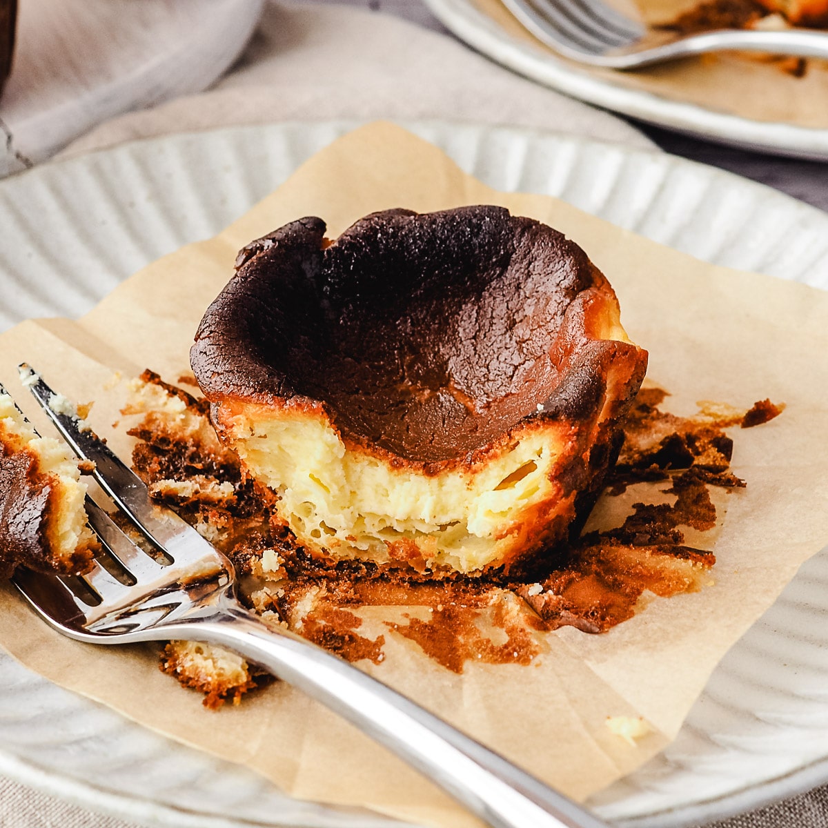 Close up mini cheesecake on a plate with a piece taken out with a fork, rest of cheesecakes in background.