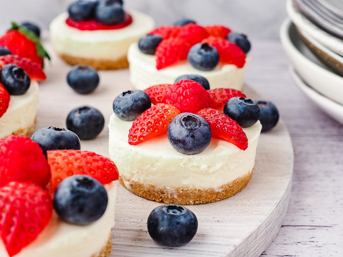 Cheesecakes on a platter with fresh fruit and stack of plates in background.