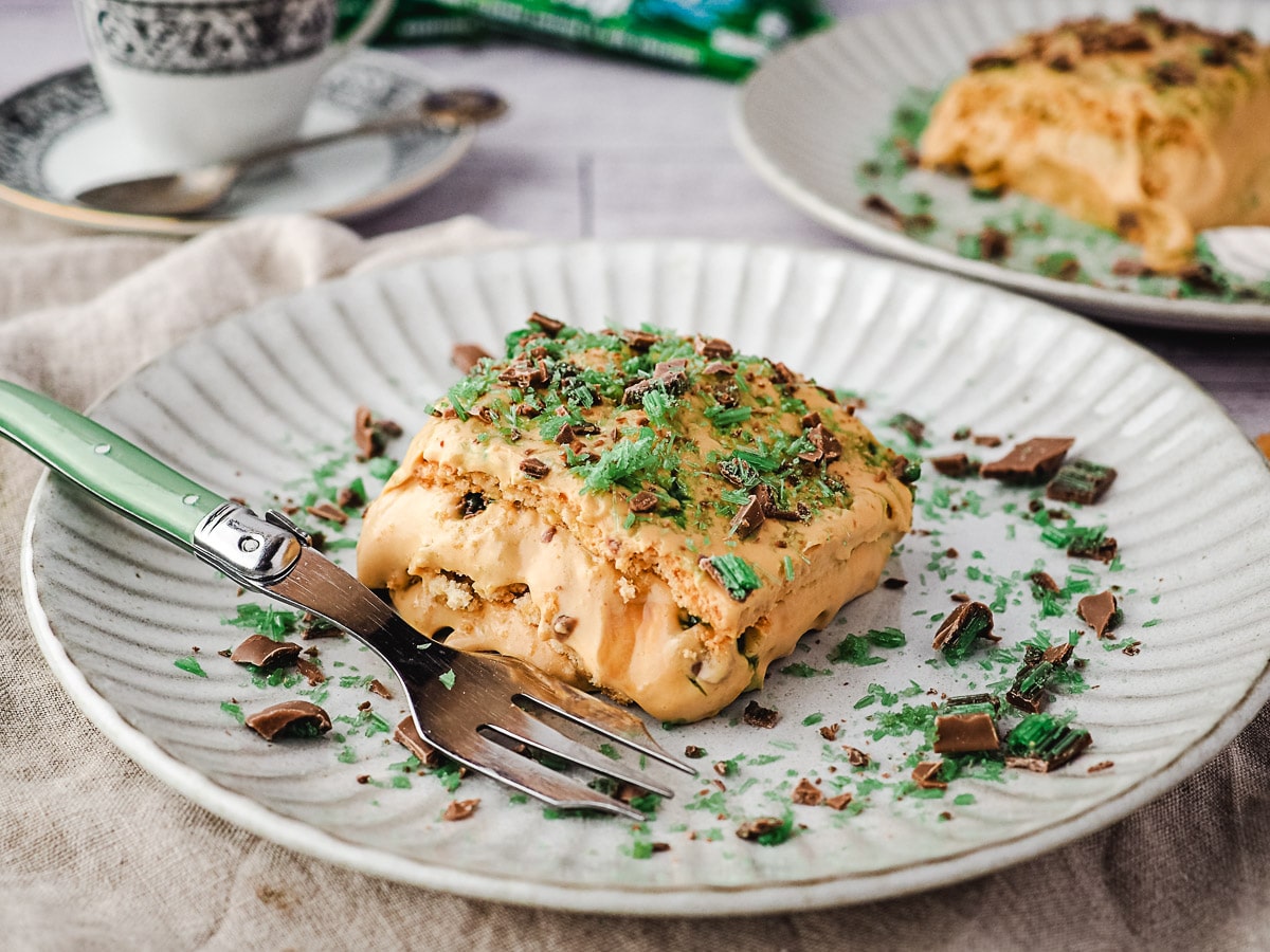 Slice of tart on a plate with a fork, with an extra slice of tart, coffee and peppermint crisp bars in the background.