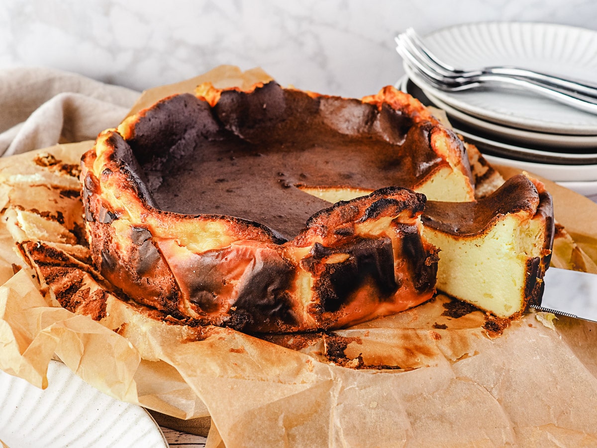 Taking a slice out of the cheesecake, with stack of plates and forks in the background.