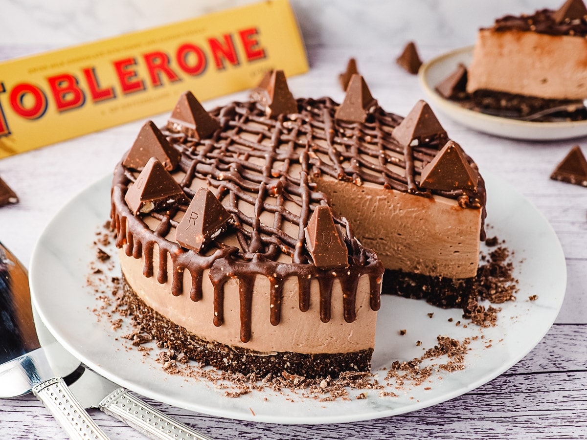 Whole cheescake on a plate, with slice on a plate and Toblerone in background.