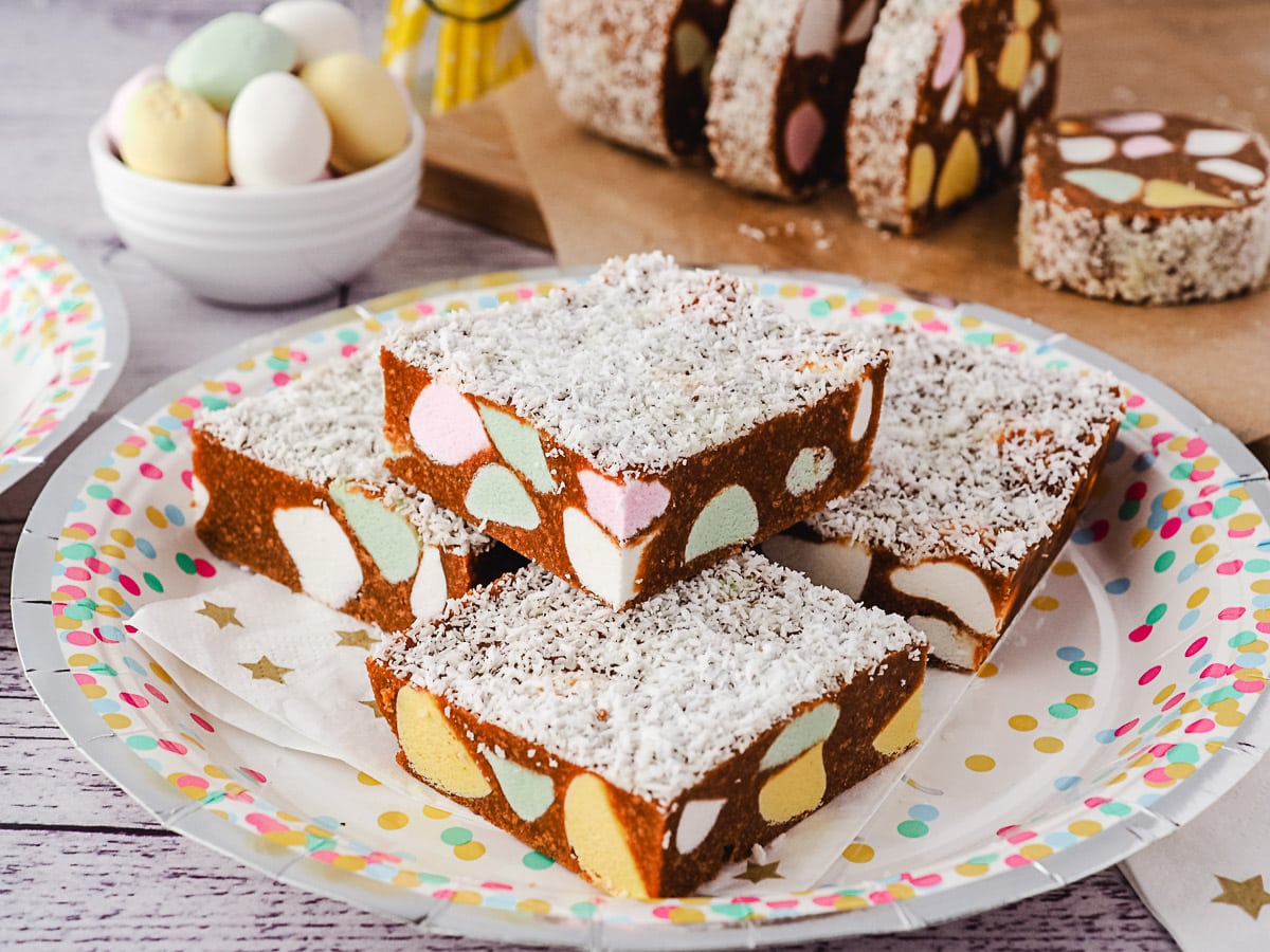 Pieces of slice piled on a plate, with lolly log and fruit puffs in background.