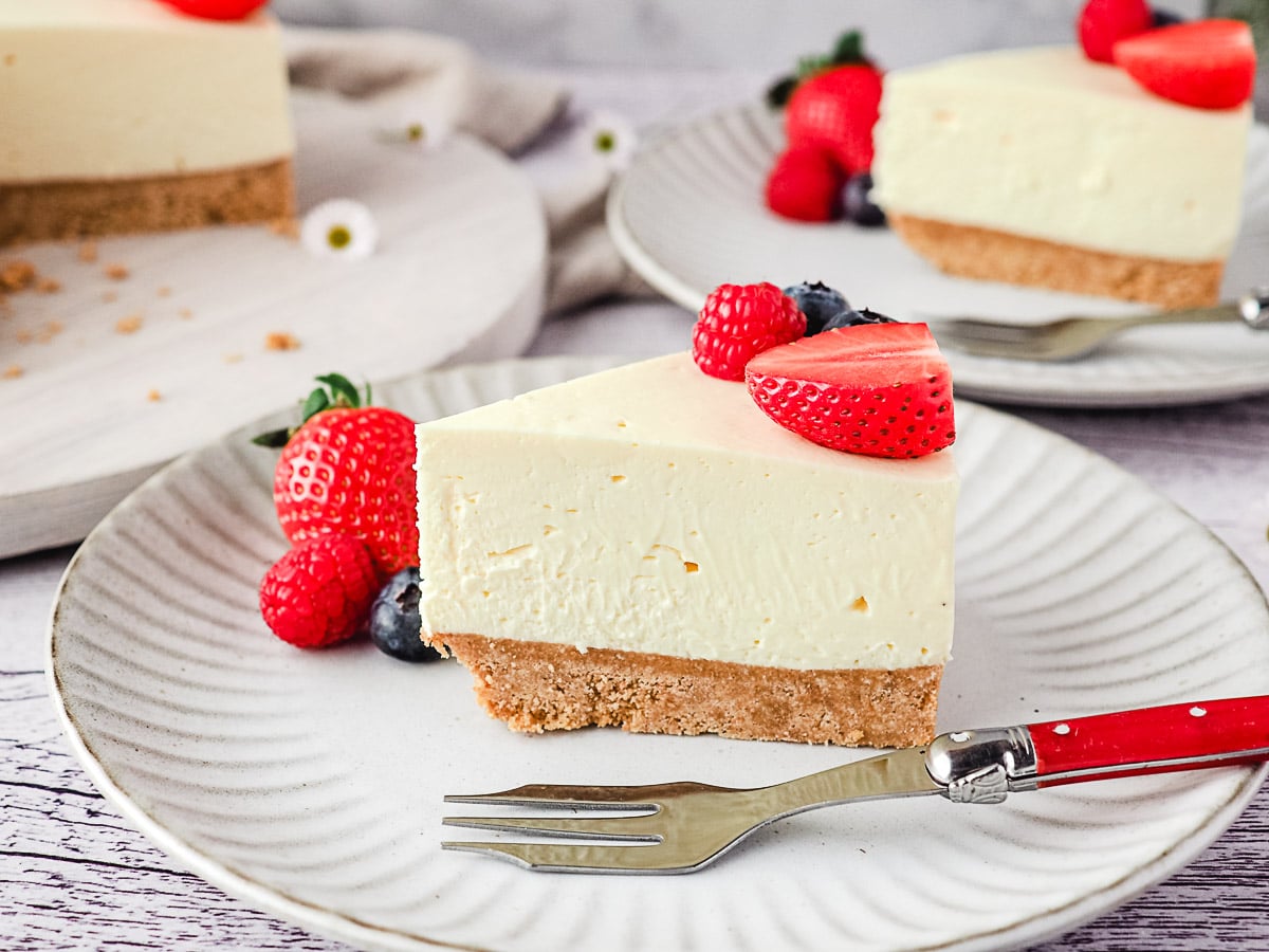 Philadelphia No Bake Cheesecake 2 Slice of cheesecake on a plate with fresh berries and rest of cake and another slice of cheesecake in the background.
