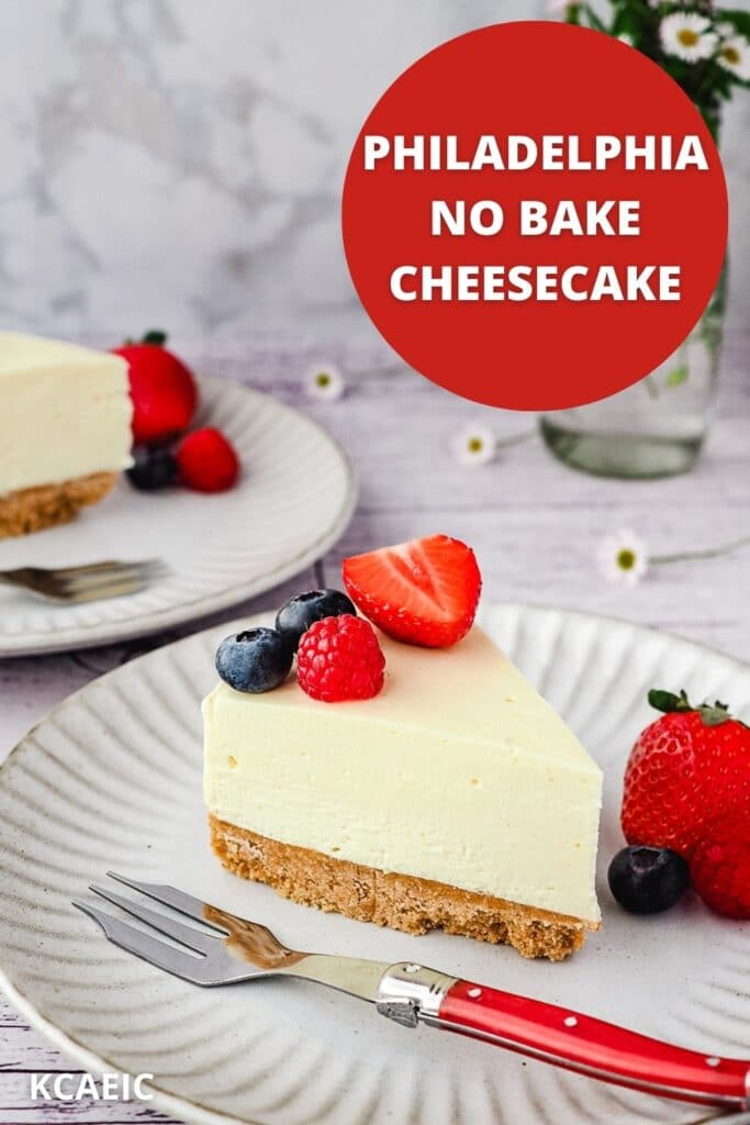 Slice of cheesecake on a plate with fresh berries, with another slice of cheesecake and small vase of flowers in the background, with text overlay.
