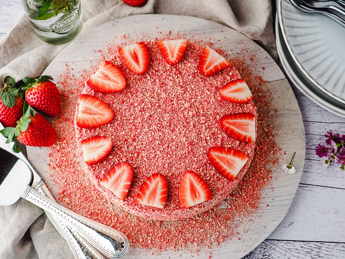 Top down view of cheesecake on a board, with serving ware and fresh strawberries.