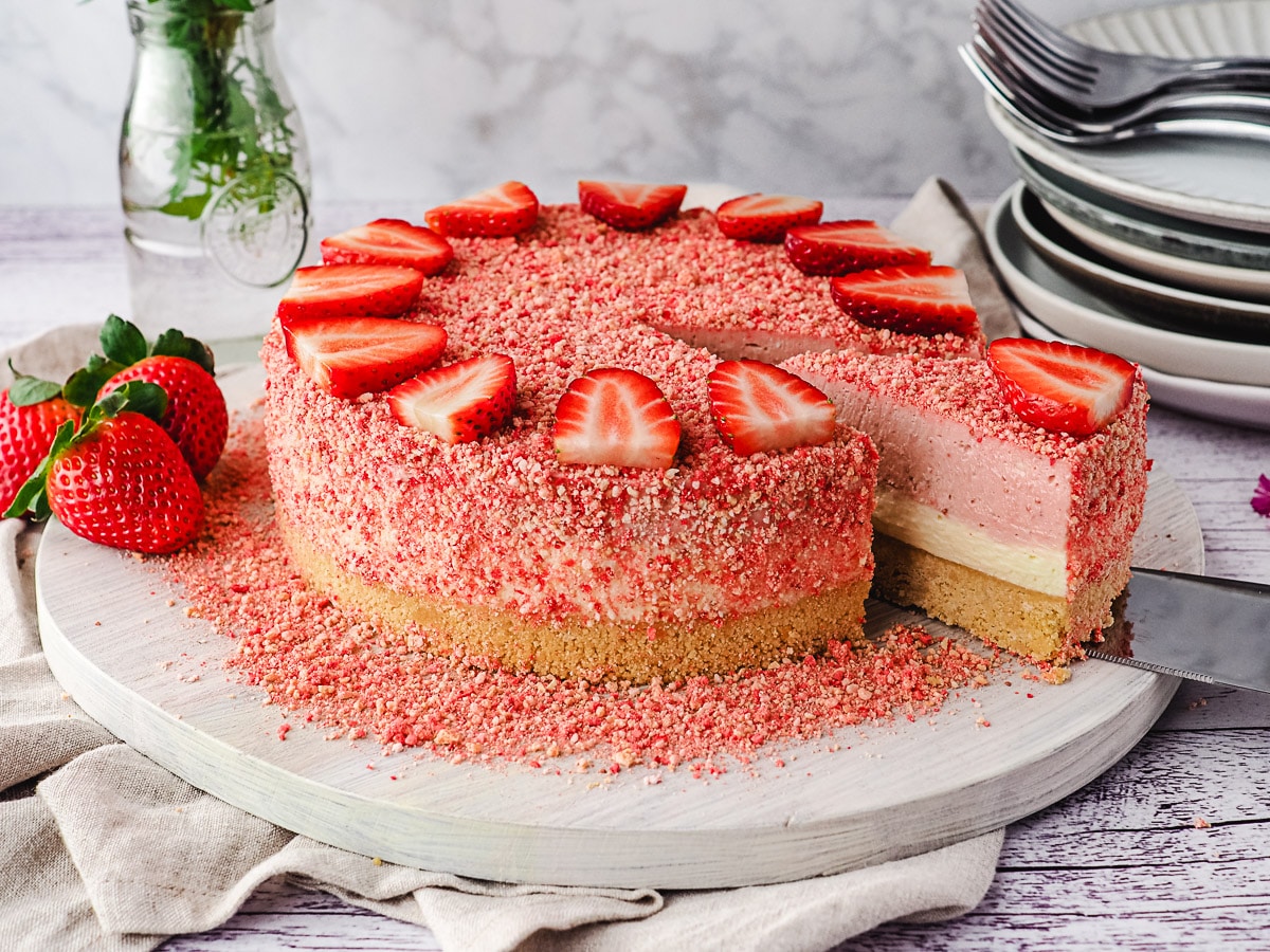 Slicing cheesecake, with fresh strawberries and stack of plates in the background.