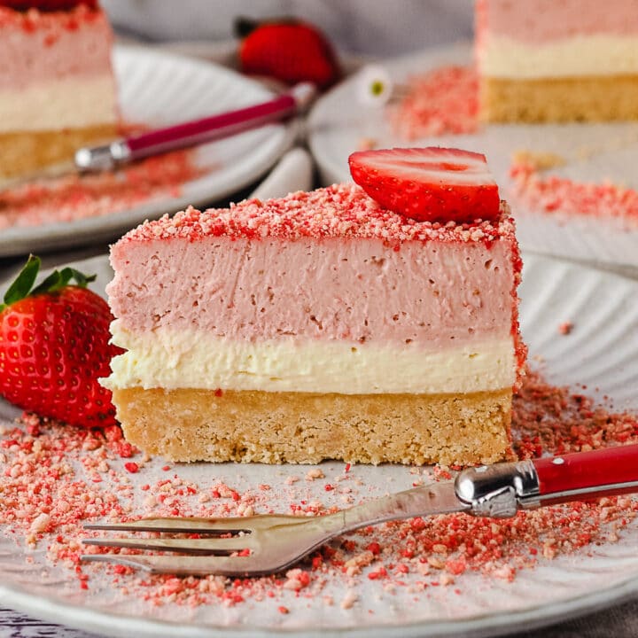 Close up slice of cheesecake on a plate with a fork, and another slice of cake and rest of cake in background.