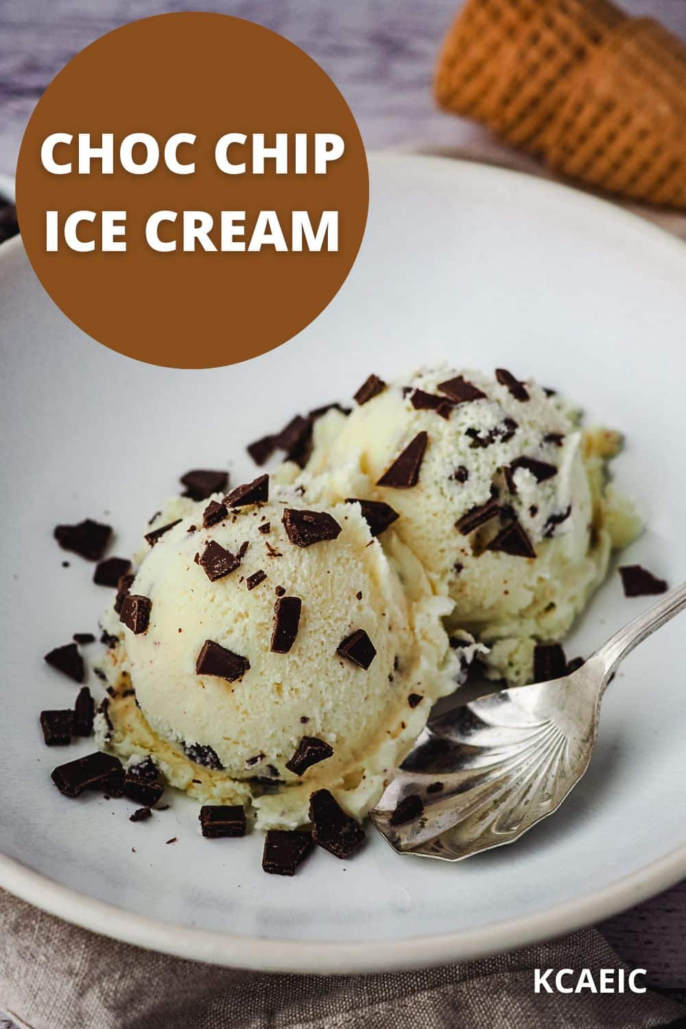 Two scoops of ice cream in a white bowl sprinkled with extra choc chips, a vintage spoon on the side, ice cream cones in the background and text overlay.