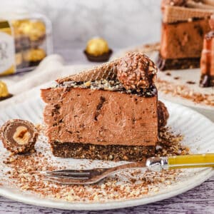 Close up slice of cheesecake on a plate with a fork, with Ferrero Rocher and rest of cheesecake in the background.