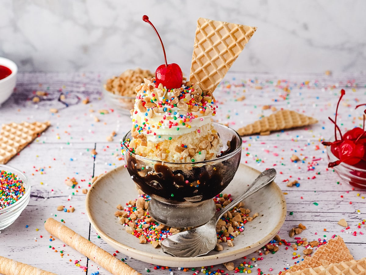 Ice Cream Sundae 9 Classic sundaes in a cup, surrounded by sprinkles, wafers, spoons, nuts and maraschino cherries.