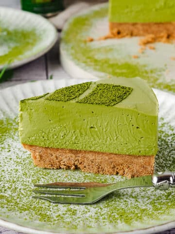 Close up slice of cake o a plate with a fork and matcha dusting.