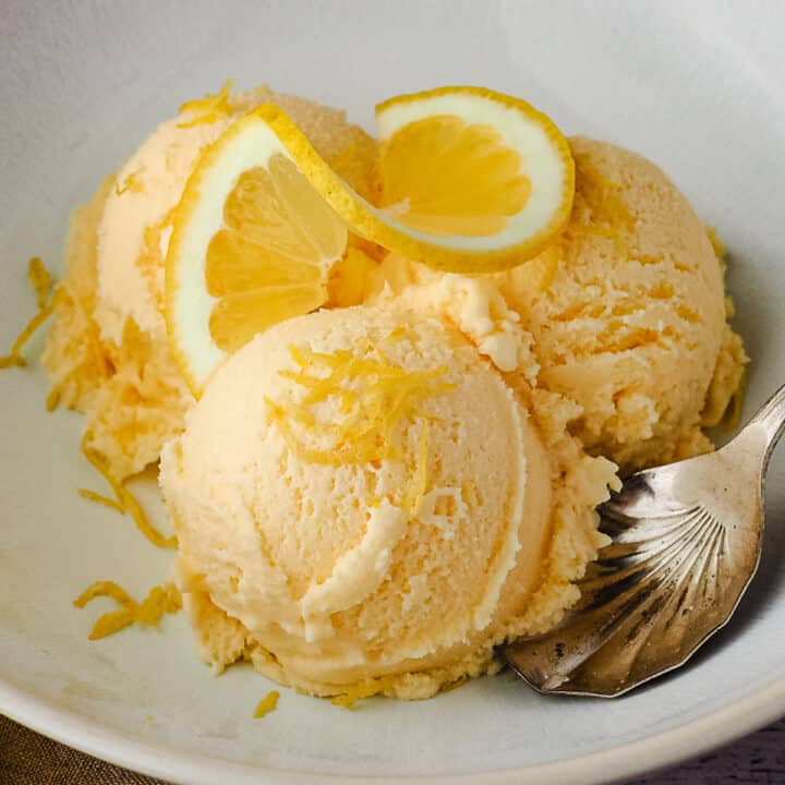 Close up three scoops of ice cream garnished with fresh lemon.