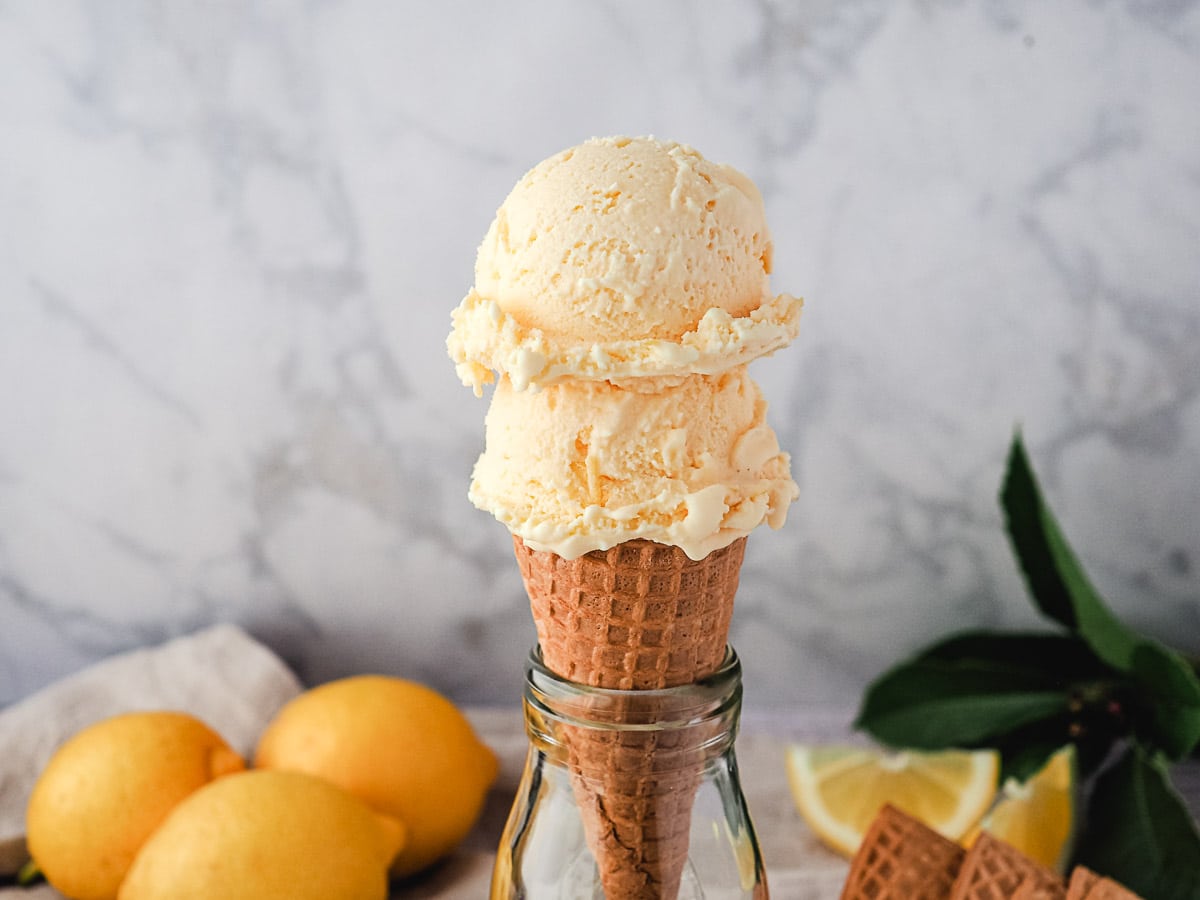 Two scoops of ice cream in a cone, with fresh lemons in the background.