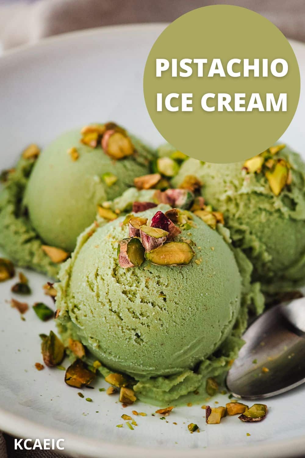 Three scoops of ice cream in a bowl topped with chopped roasted pistachios, with a spoon on the side.