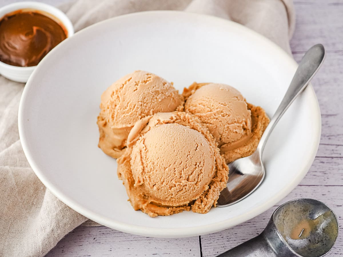 Three scoops of ice cream in a bowl with dulce de leche in background.